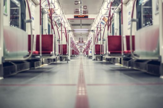 A low-angle view of an empty, modern subway train interior with red seats, offering a long perspective of the aisle.