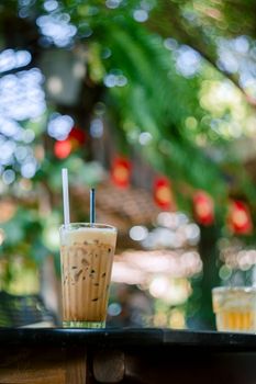 Glass of iced coffee with cream on a table outdoors, surrounded by blurred summer foliage.