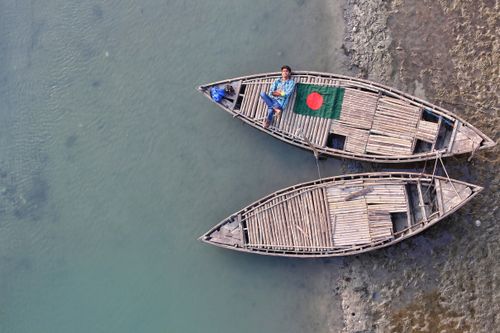 Free Aerial shot of a wooden boat with the Bangladesh flag on a calm river, showcasing tranquil Bangladeshi life. Stock Photo