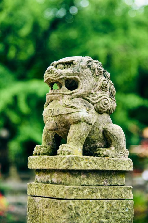Free A moss-covered stone guardian statue in a tranquil green garden. Perfect for cultural and historical projects. Stock Photo