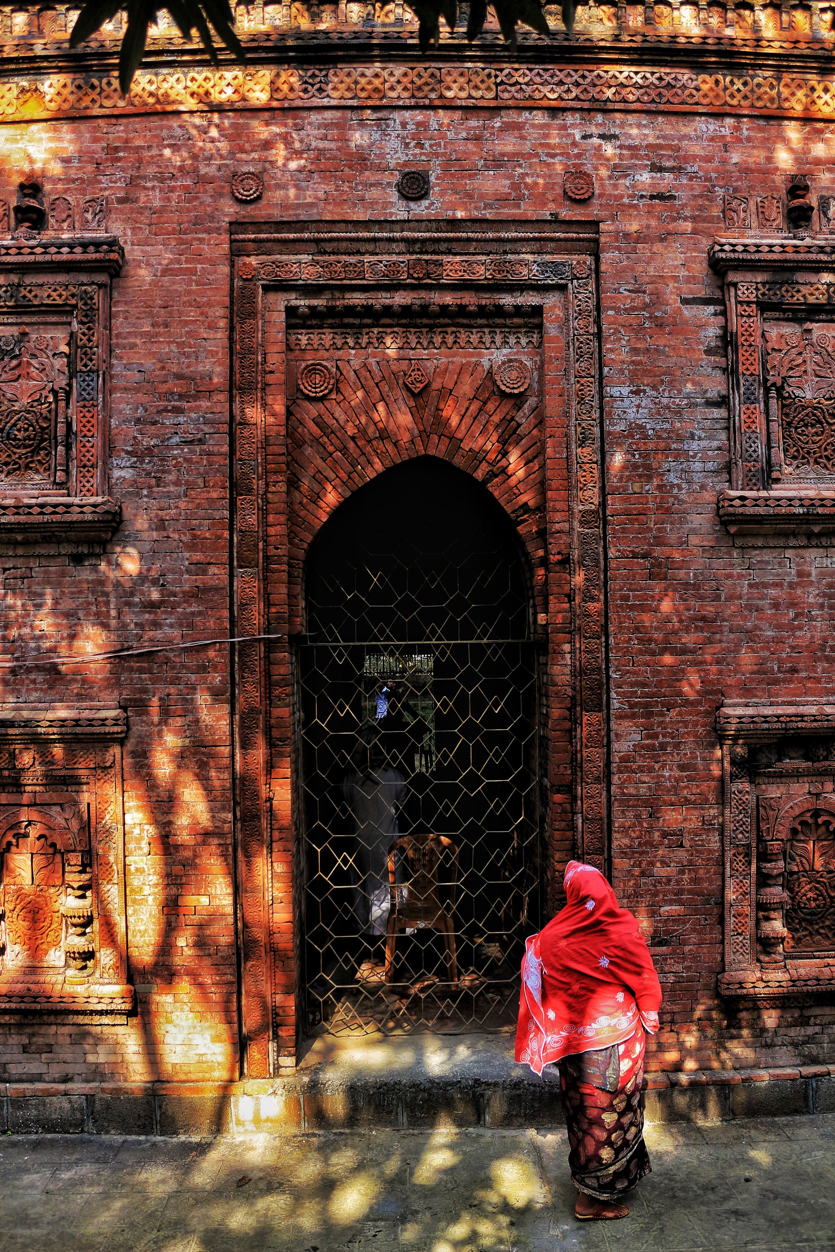 Traditional Bengal architecture with a woman in red adds vibrant contrast to historical mosque facade.