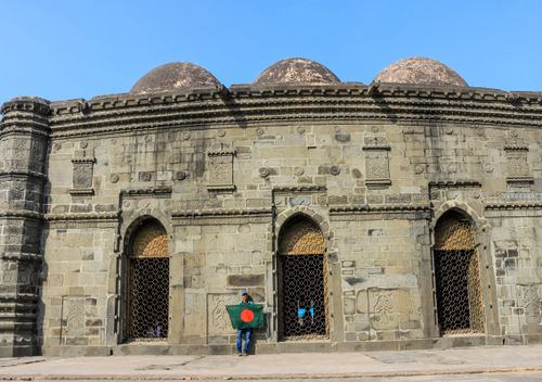 Free Historic mosque in Bangladesh with a person holding the national flag, showcasing Islamic architecture. Stock Photo