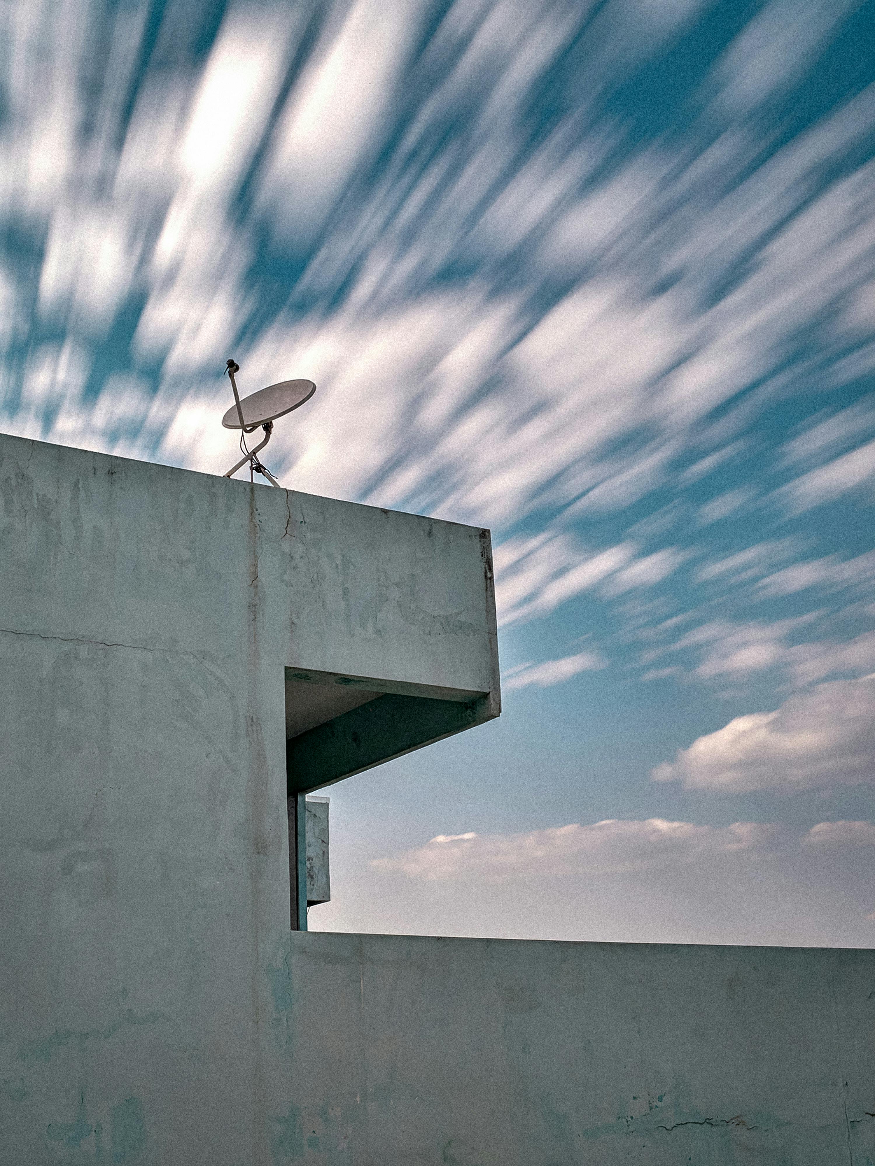 Modern building rooftop with satellite dish against a blurred cloudy sky, conveying speed and communication.