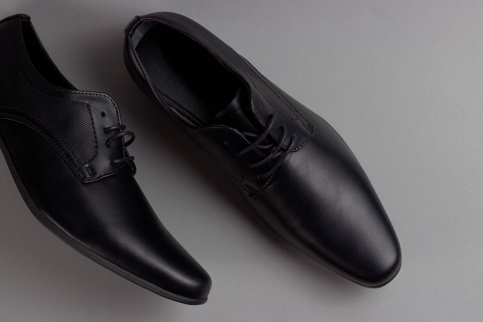 Pair of stylish black formal shoes displayed on a minimalist grey background, perfect for business attire.