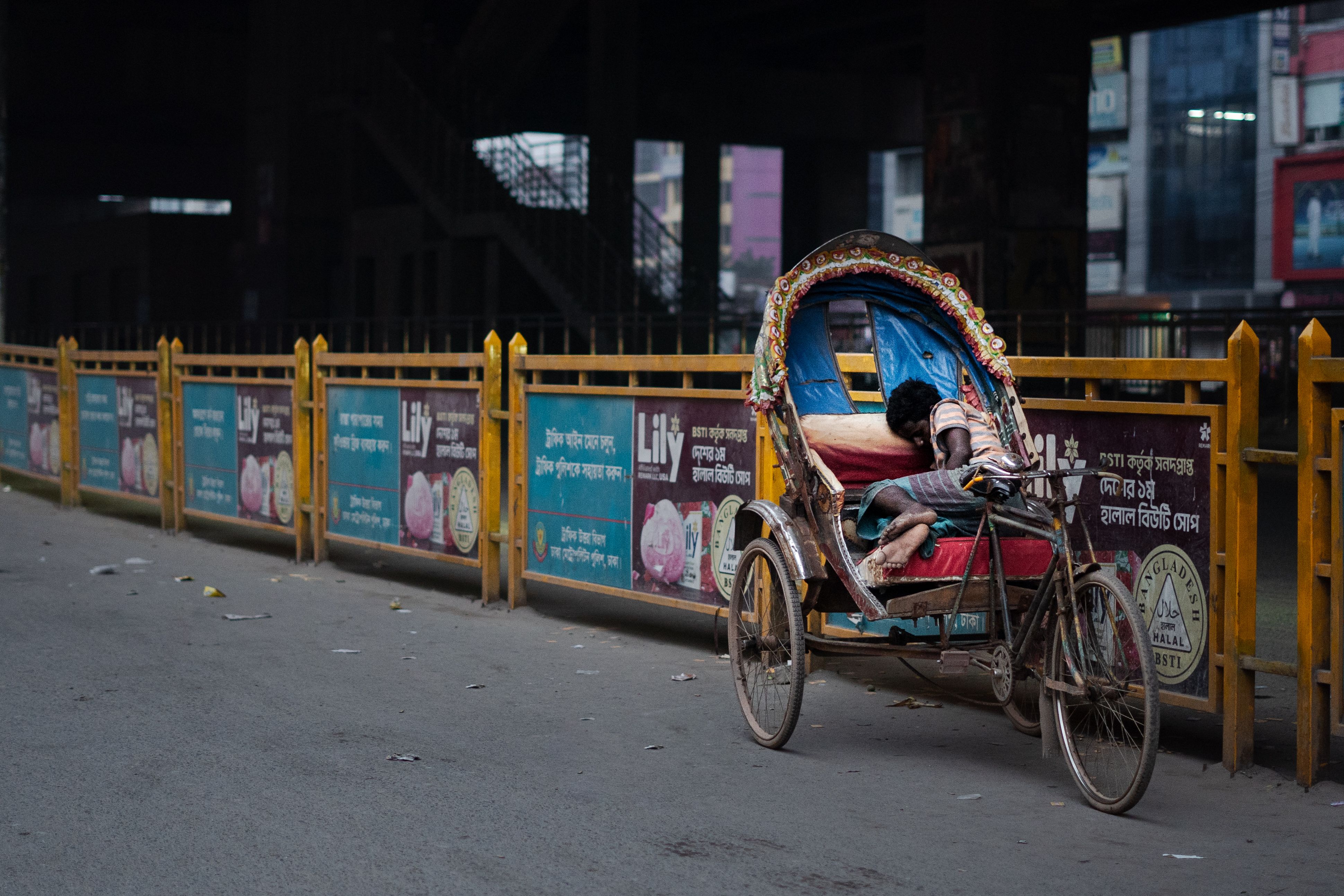 A child sleeps inside a colorful rickshaw on a quiet urban street, creating a serene scene.