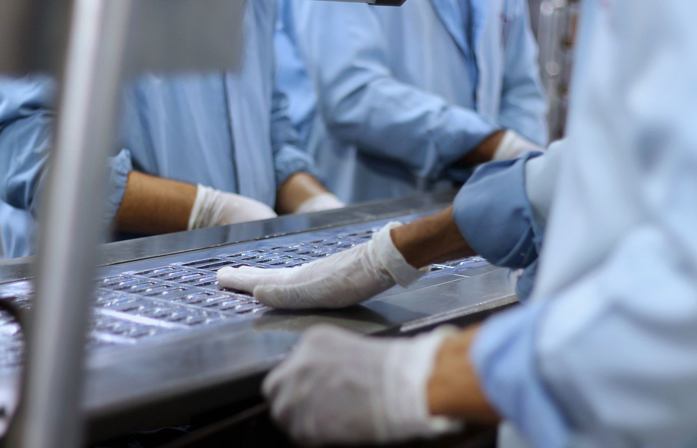 Workers on a pharmaceutical packaging line inspecting tablets in production