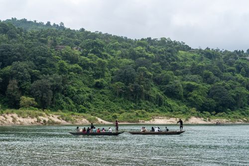 Free People enjoying a serene boat ride in a scenic river with lush green hills in the background. Stock Photo