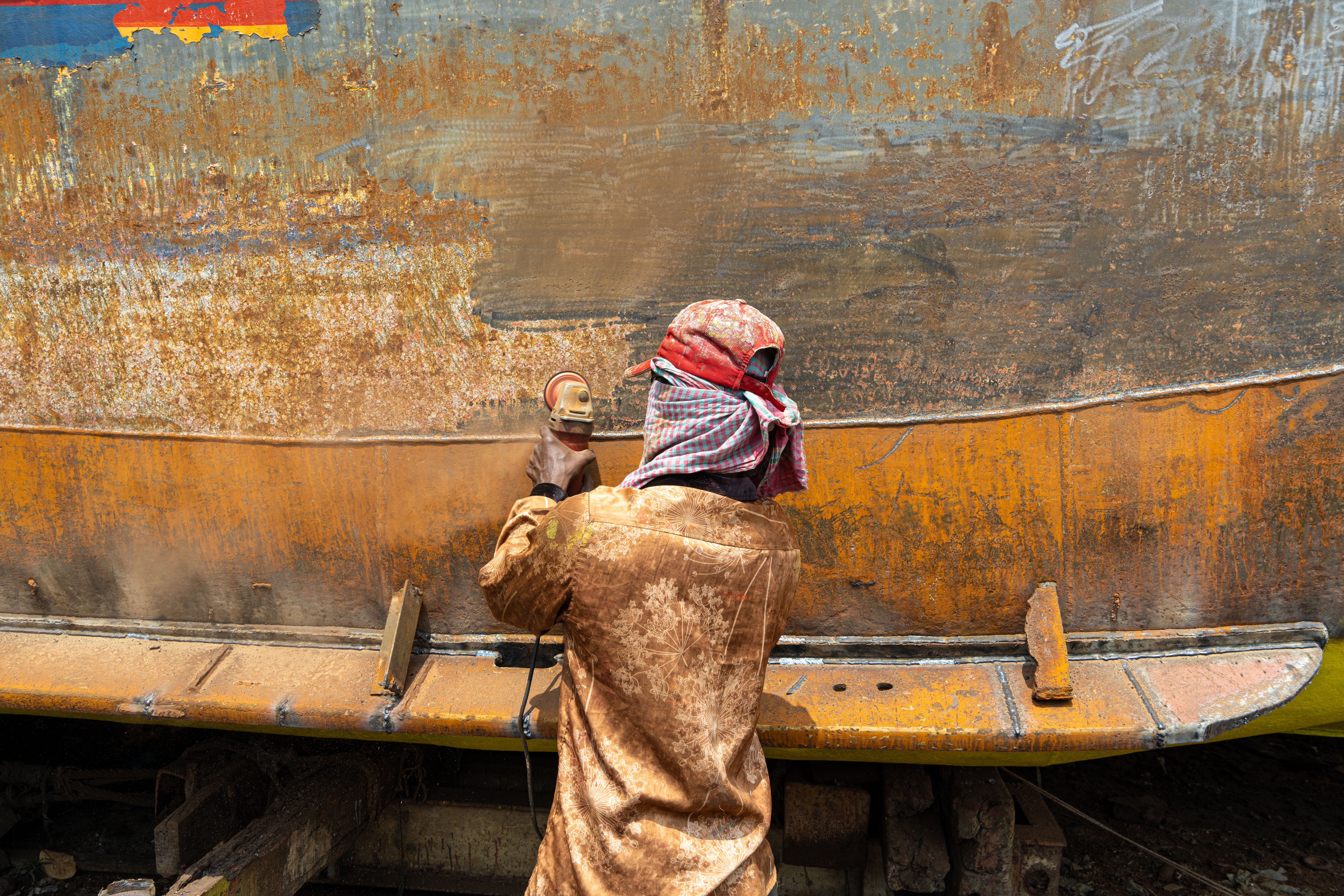 Angle grinder removing heavy rust from structural steel beam in an industrial plant