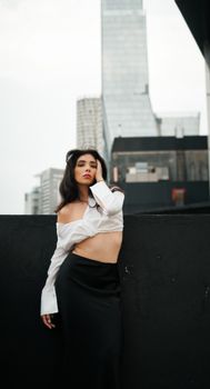 Stylish woman in off-shoulder top posing in a modern cityscape setting.