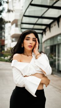 Elegant woman in white blouse posing outdoors in a modern cityscape.