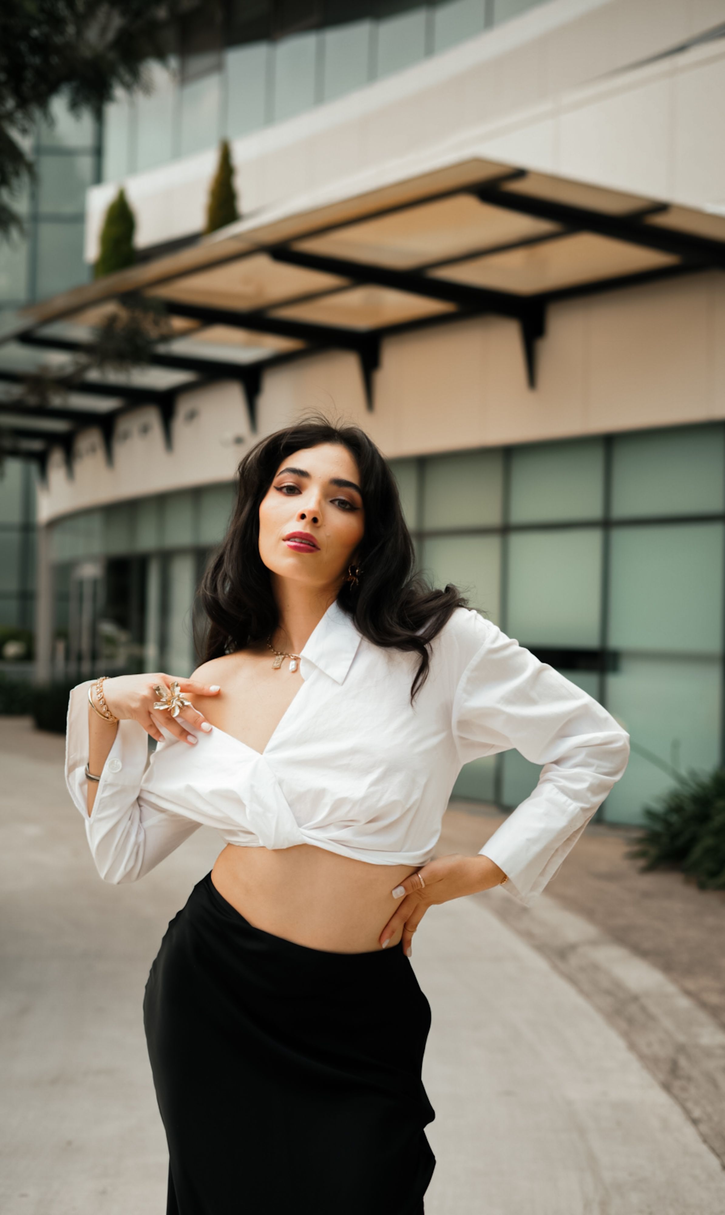 Mulher elegante posando com confiança em um ambiente urbano com arquitetura moderna.