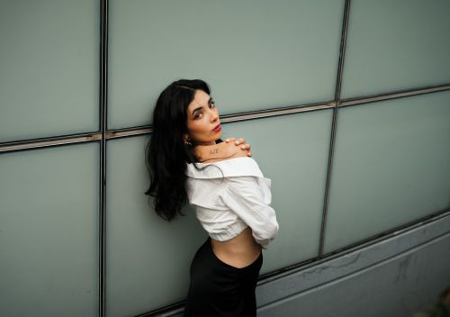 Free Confident woman with tattoo poses in chic outfit against a sleek wall for a fashion-forward look. Stock Photo