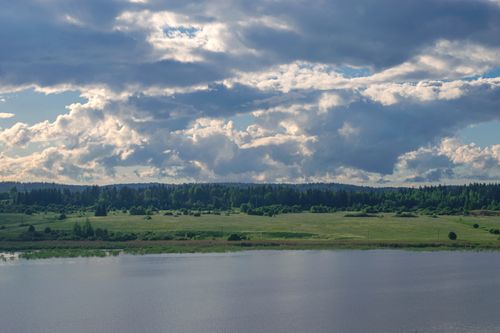 Free Idyllic Nordic countryside with lush fields and dramatic clouds over a tranquil river. Stock Photo
