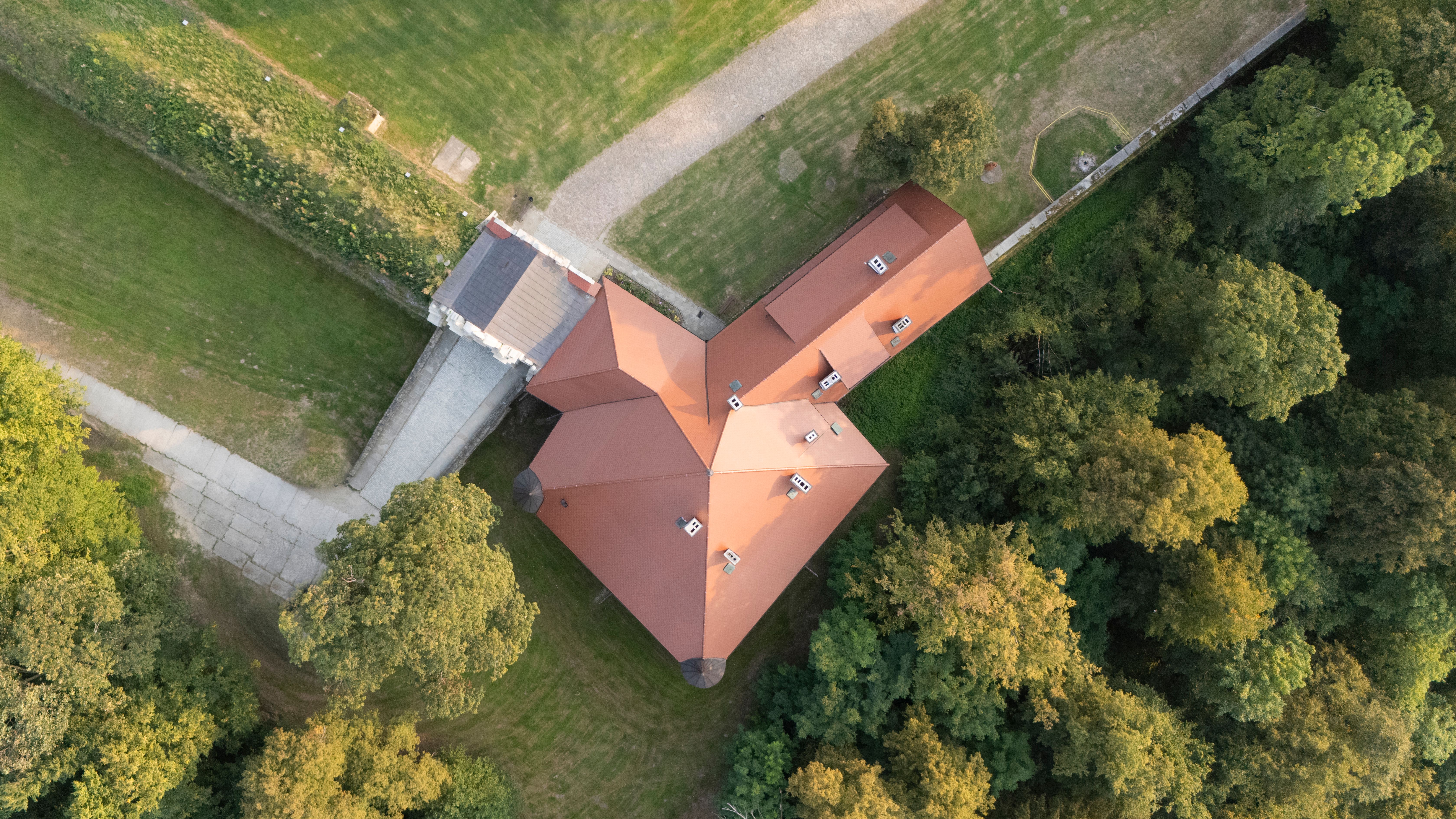 Aerial shot of a red-roofed building surrounded by lush greenery, captured from above.