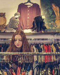 A woman explores racks of clothing in a cozy vintage shop with eclectic decor.