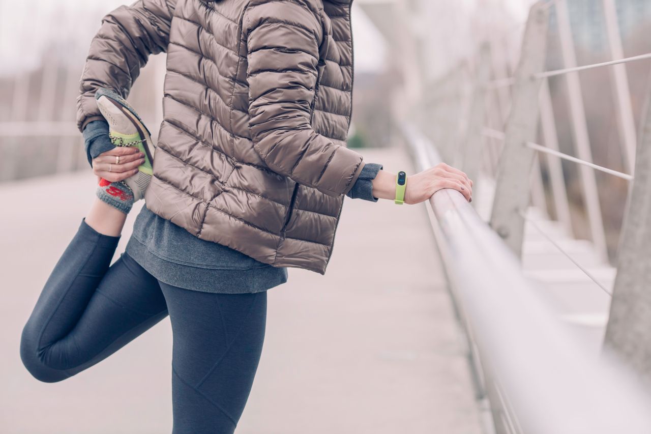 Woman in a puffer jacket and leggings stretching on a bridge