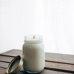 A white candle with a wooden wick in a glass jar on a wooden bench