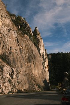 A picturesque view of a mountain road surrounded by towering rocky cliffs under a bright blue sky.