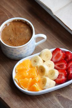 Colorful fruit platter with bananas, strawberries, oranges, and coffee on wooden table.