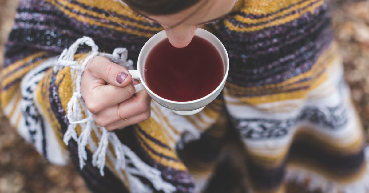 A woman wrapped in a cozy blanket enjoying a hot beverage outdoors during fall.