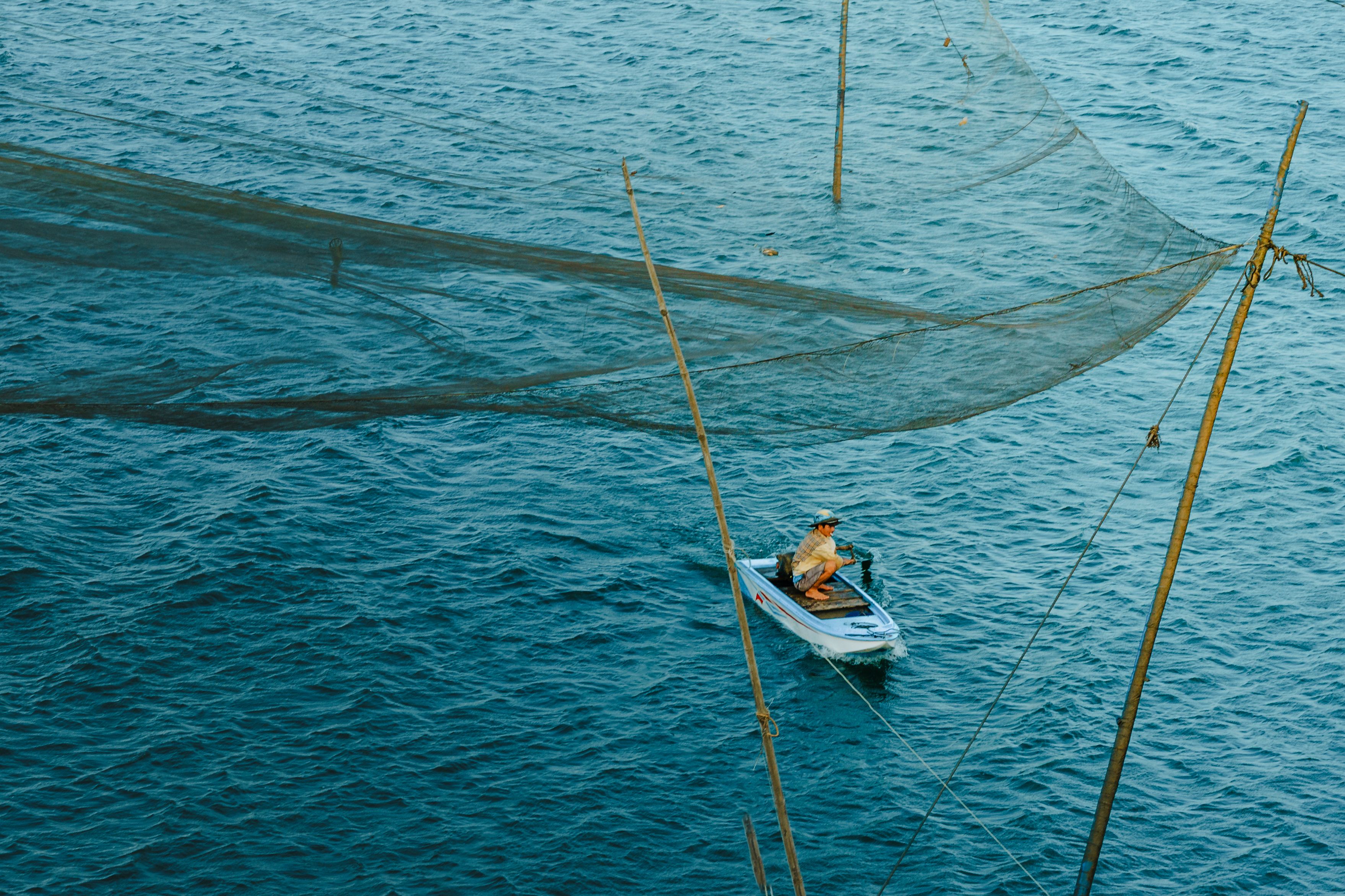 Fisherman on Boat Beside Large Fishnet in Blue Water · Free Stock Photo