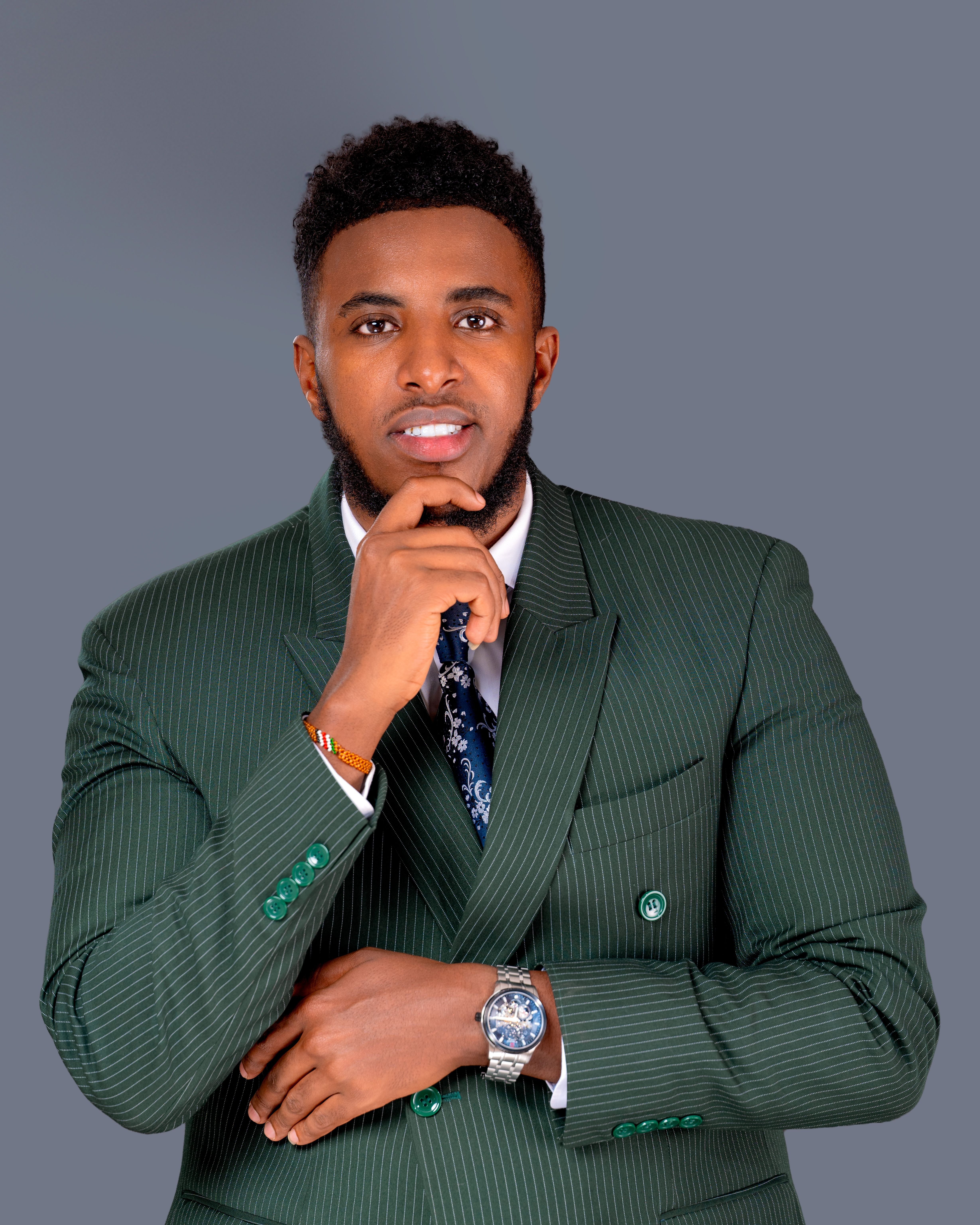 Portrait of a confident man in a green pinstripe suit against a neutral gray background.
