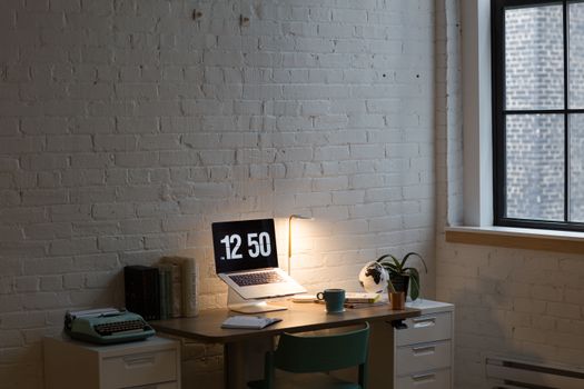Cozy workspace with a laptop, lamp, and books on a wooden desk against a brick wall.