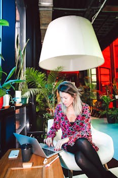 一位身穿花卉连衣裙的年轻女子，在灯光明亮的时尚休息室里用笔记本电脑工作