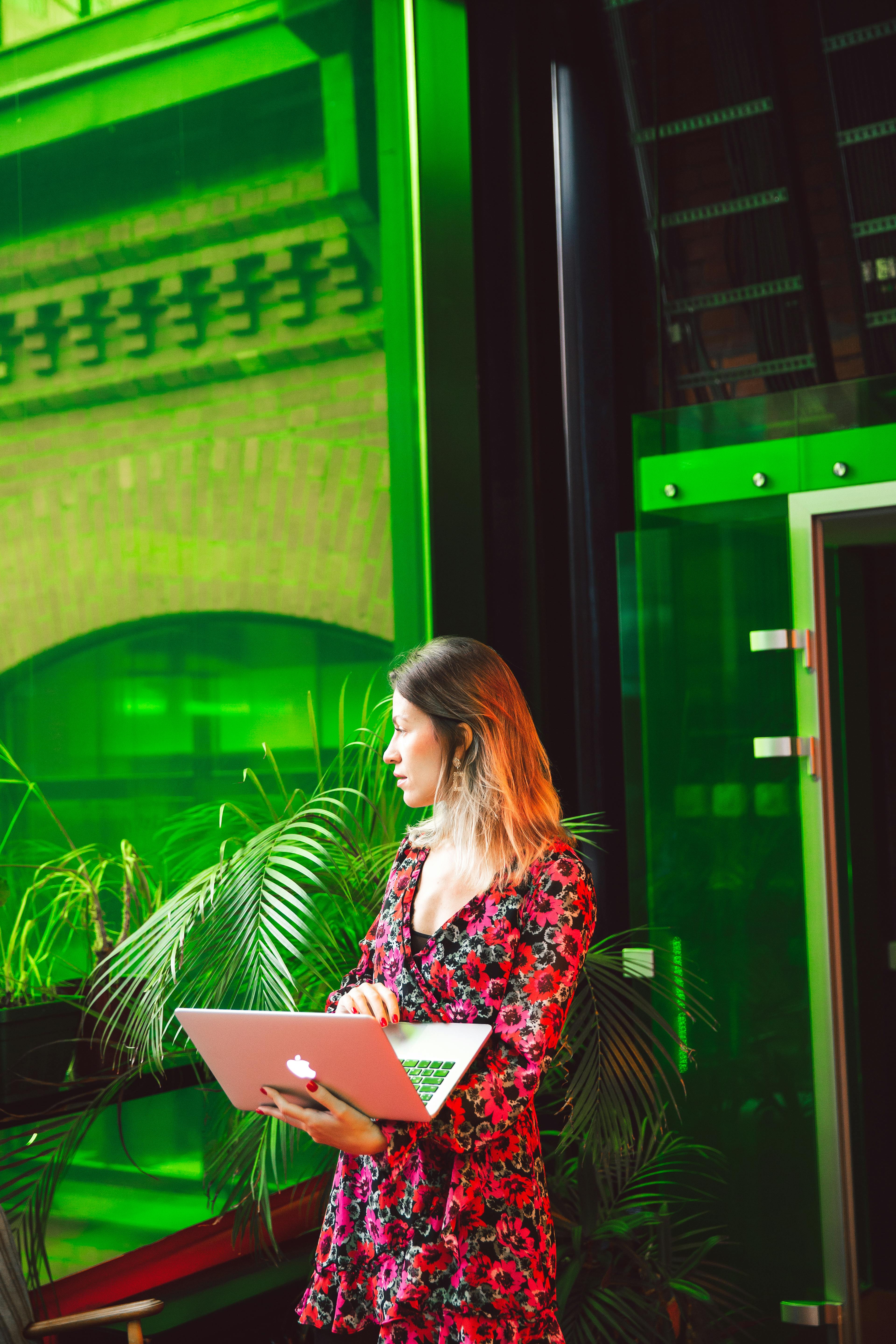 一名女子坐在色彩缤纷的办公室里，手持笔记本电脑，目光移开，周围环绕着绿色装饰