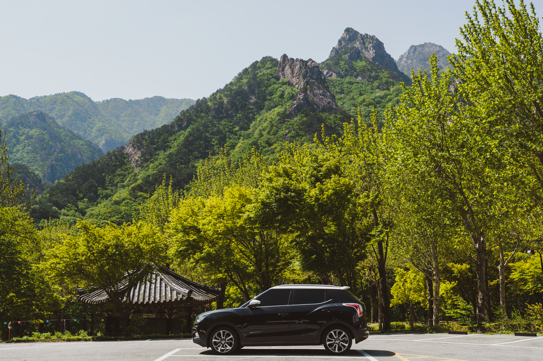 Black SUV parked against a lush green mountainous backdrop with clear skies.