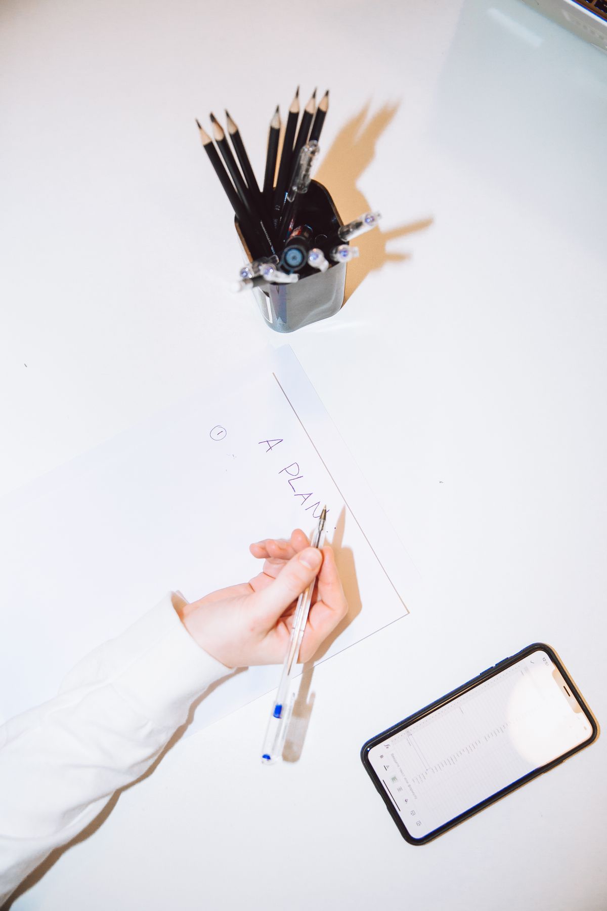 Top view of person writing in a notebook near a laptop and smartphone