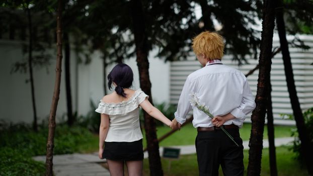 Back view of a couple walking hand in hand in a serene garden setting.