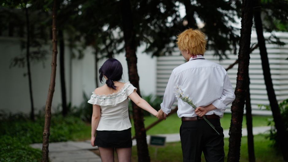 Back view of a couple walking hand in hand in a serene garden setting.