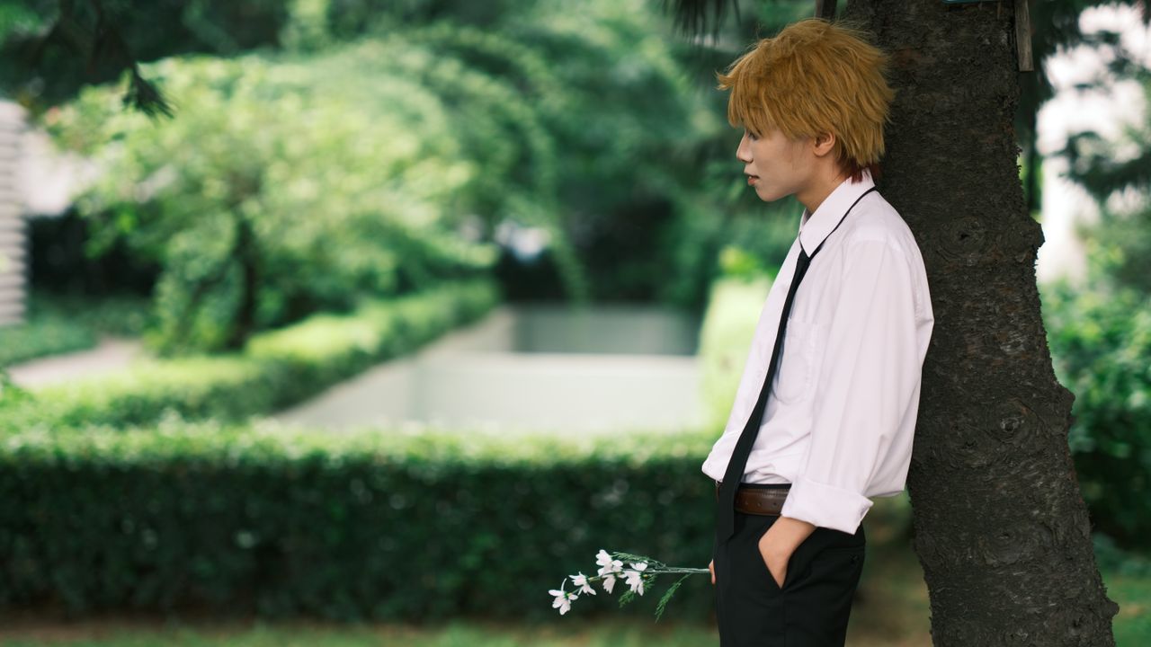 person leaning against a tree holding flowers captured in a serene gre