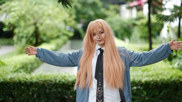 Cosplayer in a long wig and costume posing with open arms outdoors.