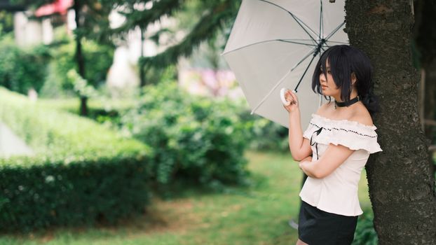 A thoughtful young woman holding an umbrella in a serene garden, embodying tranquility and style.