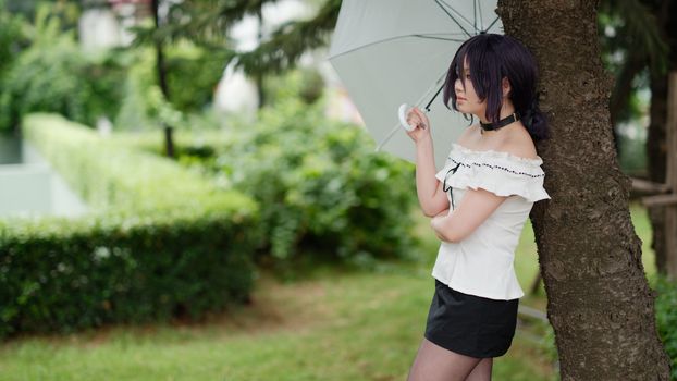 Woman with umbrella standing by a tree in a green park.