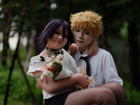 A couple in anime-style cosplay poses outdoors, with a bouquet and a warm embrace.