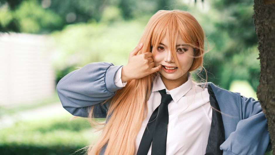 Young woman in cosplay with long wig and costume smiling in a park.
