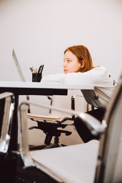 Free A woman in a modern office space appears contemplative, leaning on a desk. Stock Photo