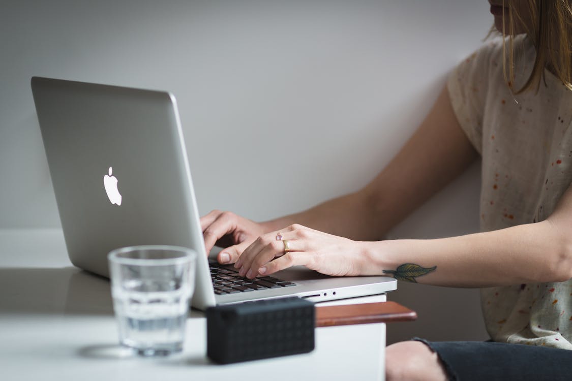 Woman Using Silver Macbook Near Shot Glass on Table