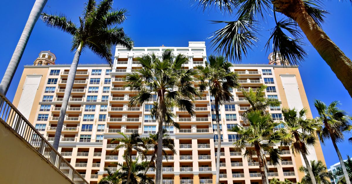 Palm trees frame the view of a luxury hotel building in Sarasota, Florida, under a bright blue sky.