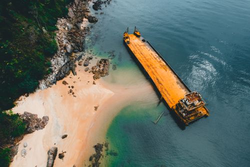 Free Drone shot of an abandoned shipwreck on a remote sandy beach, surrounded by rocky cliffs and turquoise waters. Stock Photo