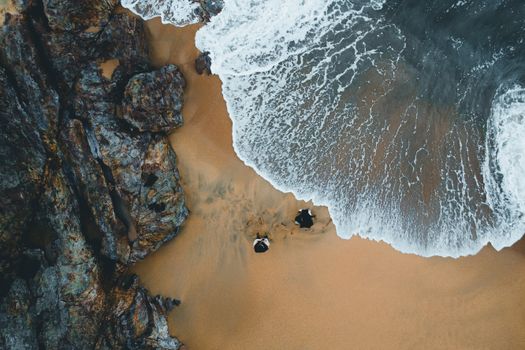 Dramatic aerial shot of a rugged coastline with waves crashing on the sandy beach, perfect for travel themes.