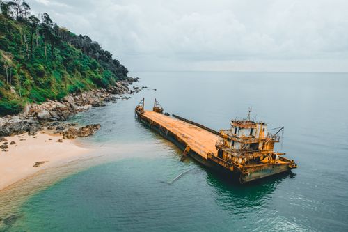 Free Aerial view of a rusted shipwreck on a tropical coastline with lush greenery. Stock Photo