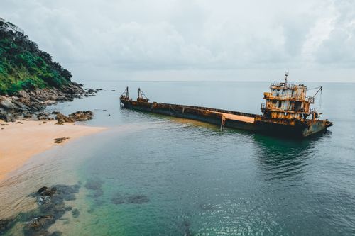 Free Aerial view of an abandoned shipwreck on a serene beach with lush green cliffs and calm sea. Stock Photo