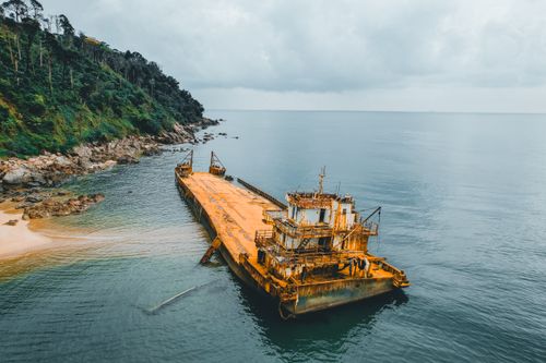 Free Aerial view of a rusty shipwreck near a jungle coastline on a cloudy day. Stock Photo