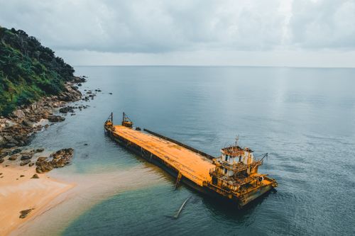 Free Aerial view of a rusted shipwreck on the coast with lush greenery and calm sea. Stock Photo
