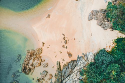 Free A breathtaking aerial view showcasing a sandy beach with rocky coastline and lush greenery, perfect for travel themes. Stock Photo
