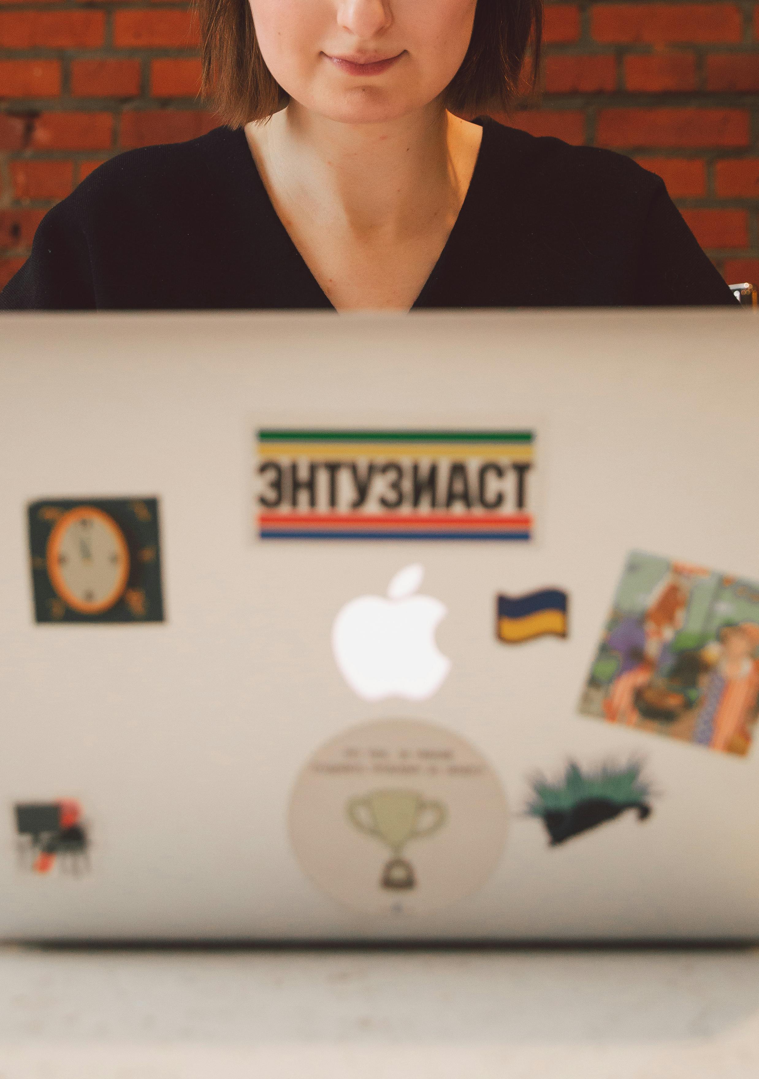 一位年轻女性在家工作，使用着贴有贴纸的笔记本电脑，这突显了远程工作与创造力